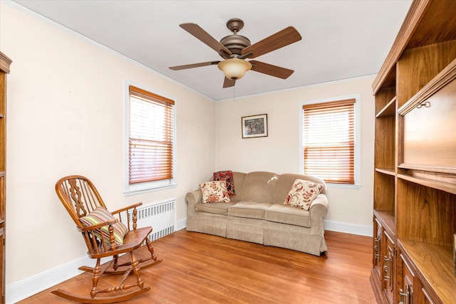 living area featuring ceiling fan, baseboards, radiator, ornamental molding, and light wood-style flooring