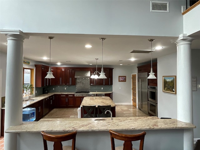 kitchen with wall chimney exhaust hood, visible vents, ornate columns, and tasteful backsplash
