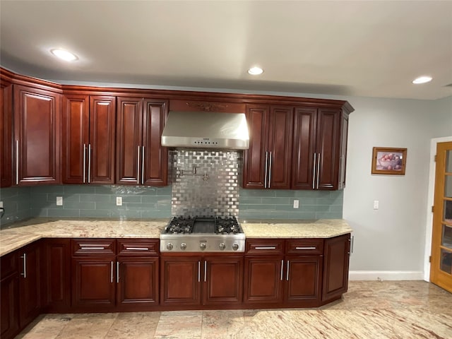 kitchen with stainless steel gas stovetop, backsplash, wall chimney range hood, light stone countertops, and baseboards