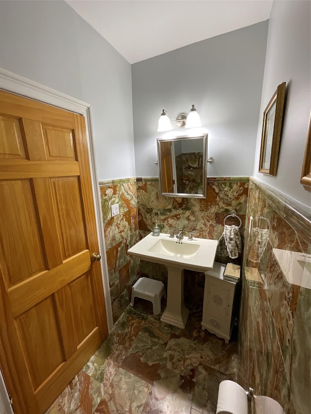 half bathroom with marble finish floor, a wainscoted wall, and tile walls