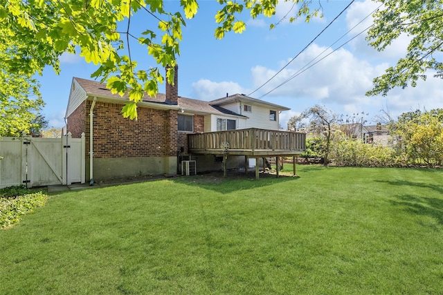 back of property featuring brick siding, a wooden deck, a gate, a chimney, and a lawn