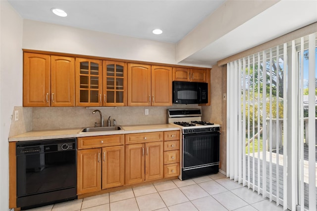 kitchen with glass insert cabinets, light countertops, a sink, light tile patterned floors, and black appliances