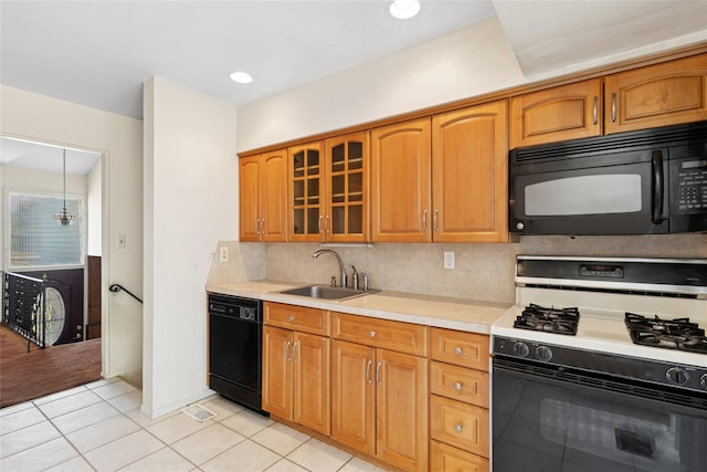 kitchen featuring glass insert cabinets, light countertops, a sink, light tile patterned floors, and black appliances