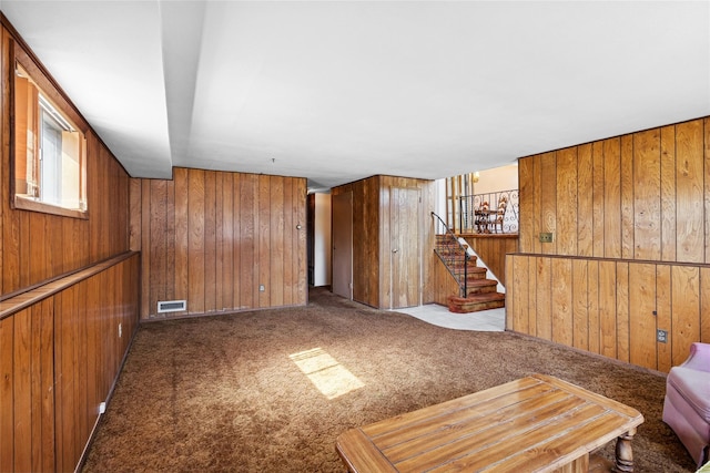 living room featuring visible vents, wood walls, stairs, and carpet floors