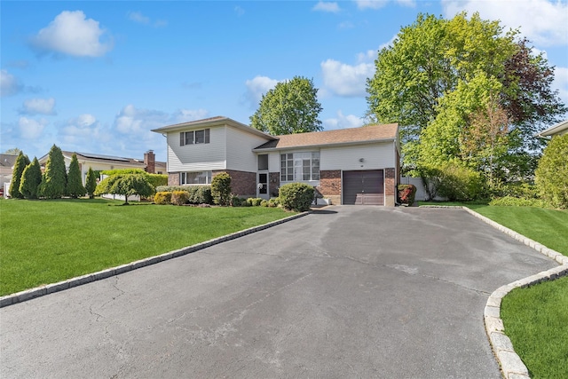 split level home featuring a garage, aphalt driveway, a front lawn, and brick siding