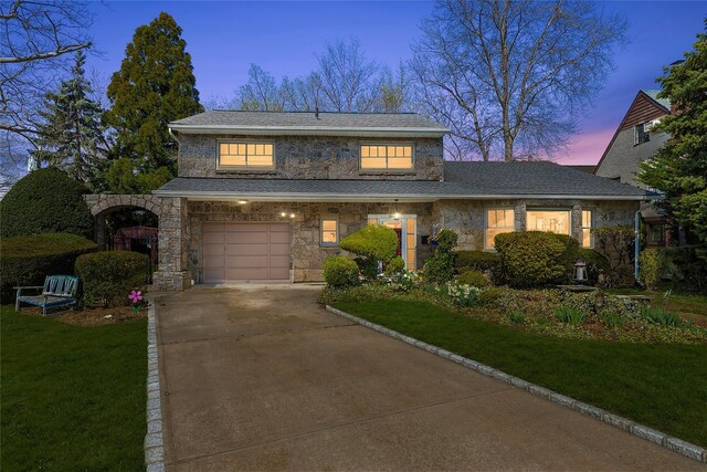 view of front of house with driveway, stone siding, a lawn, roof with shingles, and a garage