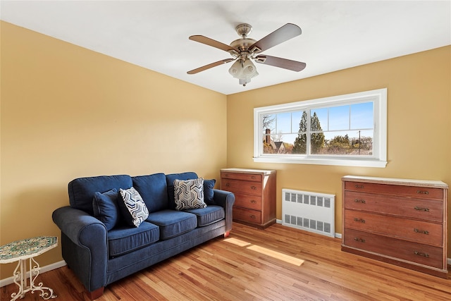 sitting room featuring light wood-type flooring, baseboards, ceiling fan, and radiator