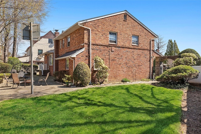 view of home's exterior with fence, a lawn, brick siding, and a patio