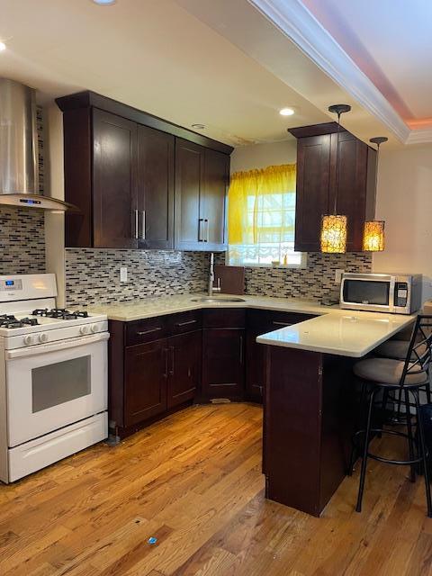 1255 E 223rd St, Bronx, NY 10466 - kitchen featuring a sink, wall chimney exhaust hood, white gas range, a peninsula, and stainless steel microwave