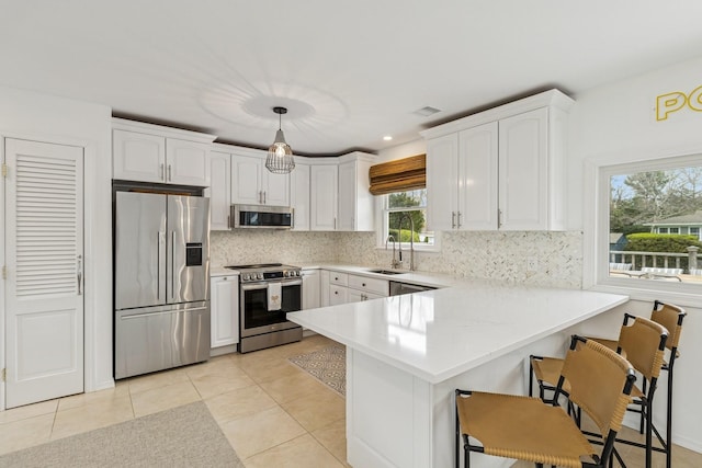 kitchen with white cabinets, a peninsula, a kitchen breakfast bar, light countertops, and appliances with stainless steel finishes