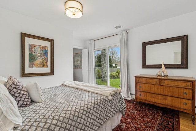 bedroom with baseboard heating, access to outside, wood finished floors, and visible vents