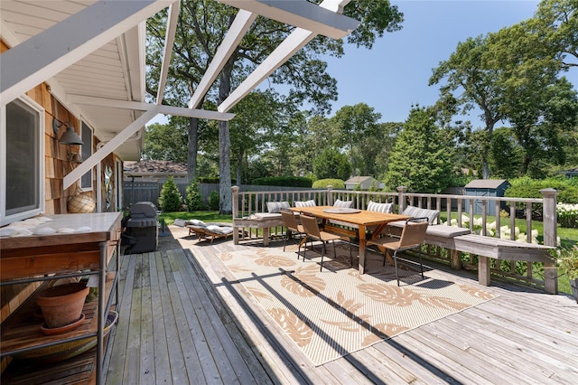 wooden terrace with fence, an outbuilding, outdoor dining space, and a storage unit