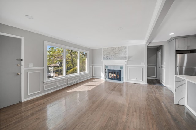 unfurnished living room with a fireplace with flush hearth, a decorative wall, visible vents, wood finished floors, and wainscoting