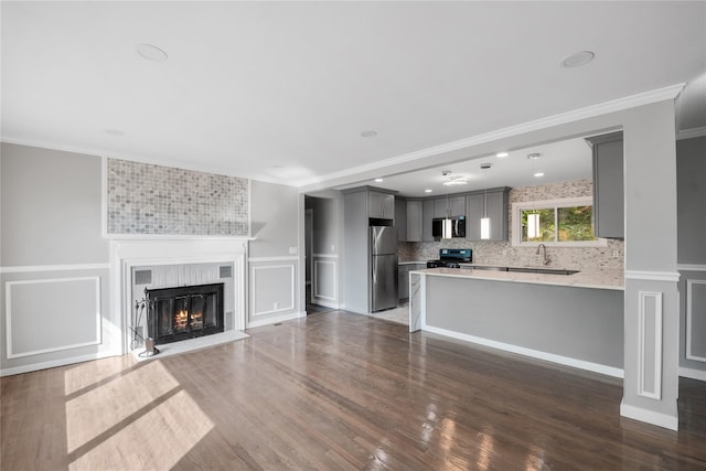 unfurnished living room with a tile fireplace, a sink, dark wood-style flooring, crown molding, and a decorative wall
