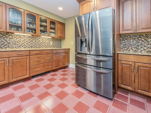 kitchen featuring backsplash, light stone counters, stainless steel fridge with ice dispenser, and glass insert cabinets