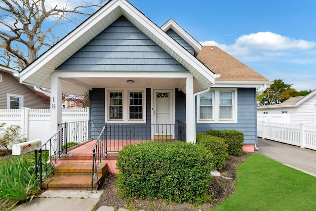 bungalow-style house featuring a shingled roof, covered porch, and fence