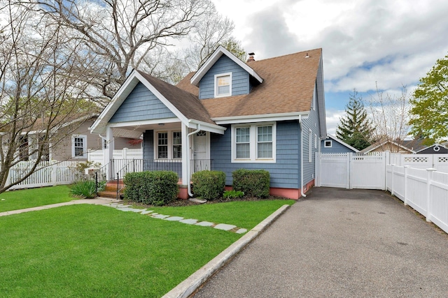 bungalow-style home with a chimney, covered porch, a shingled roof, a detached garage, and a front lawn
