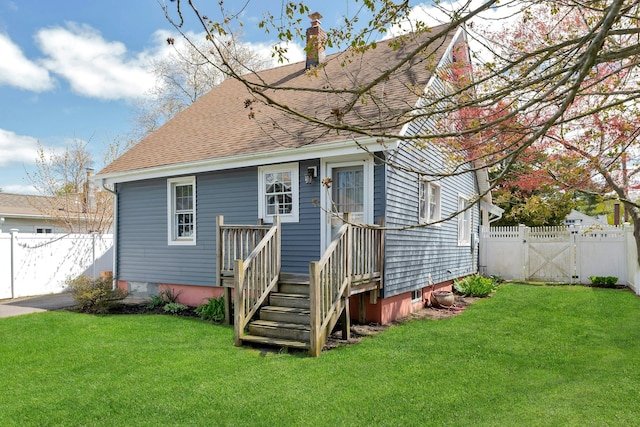 rear view of house featuring a chimney, a gate, roof with shingles, fence, and a yard