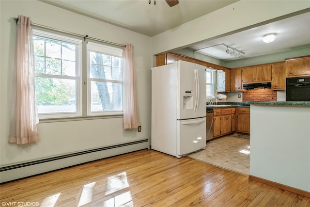kitchen with a sink, black oven, white fridge with ice dispenser, range hood, and a baseboard heating unit