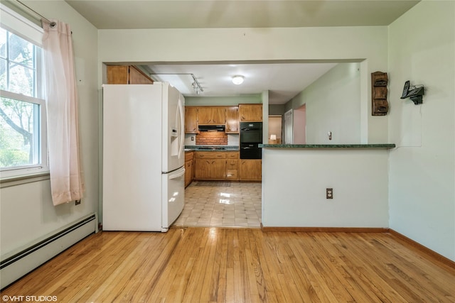 kitchen with dark countertops, baseboard heating, white refrigerator with ice dispenser, brown cabinets, and black oven