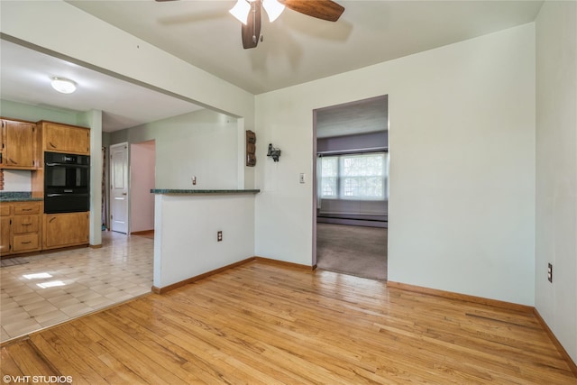 interior space with ceiling fan, a baseboard heating unit, baseboards, and light wood-style flooring