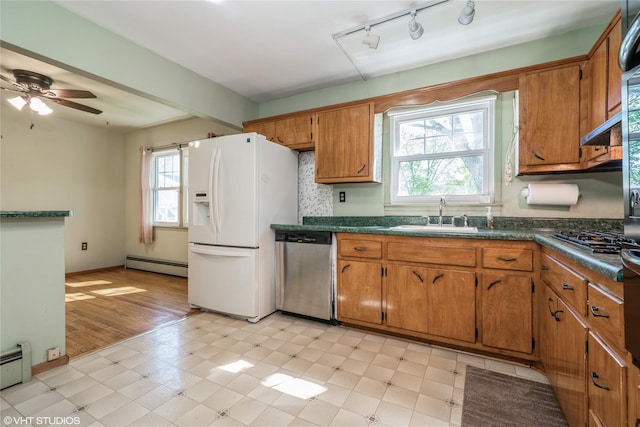 kitchen featuring dark countertops, white refrigerator with ice dispenser, baseboard heating, dishwasher, and a sink