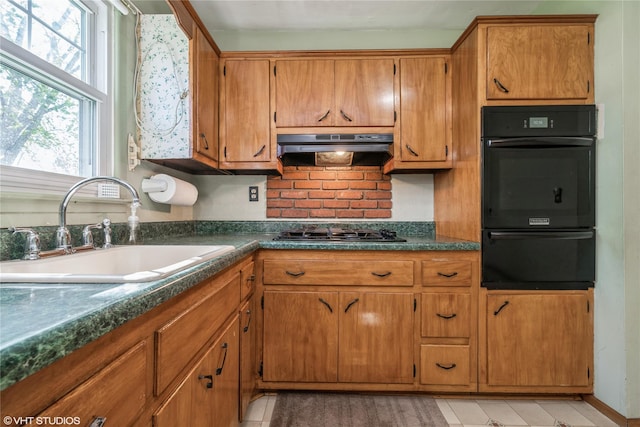 kitchen featuring gas cooktop, decorative backsplash, dark countertops, a sink, and under cabinet range hood