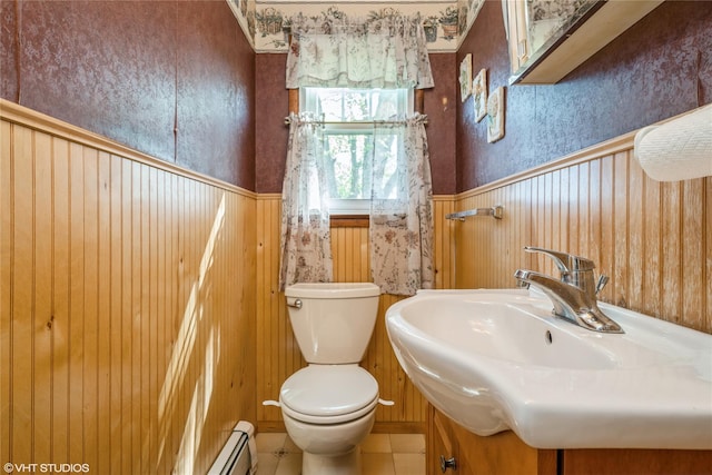 half bathroom featuring a sink, wainscoting, baseboard heating, and toilet