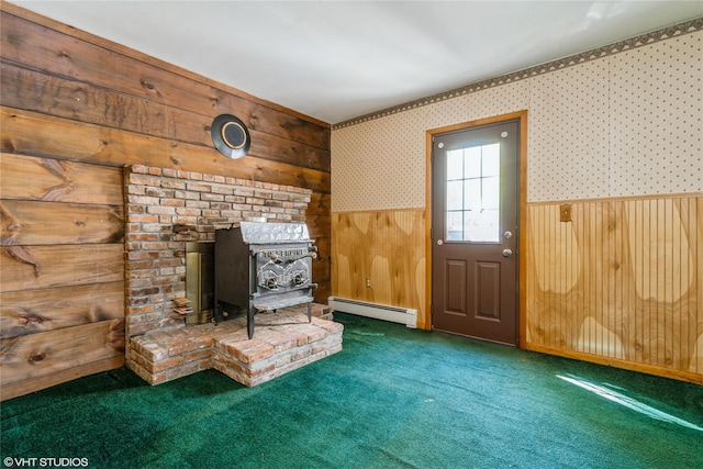 unfurnished living room featuring wainscoting, a wood stove, carpet floors, a baseboard heating unit, and wooden walls