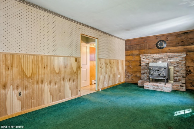 unfurnished living room featuring carpet flooring, a wood stove, wood walls, a wainscoted wall, and a baseboard radiator