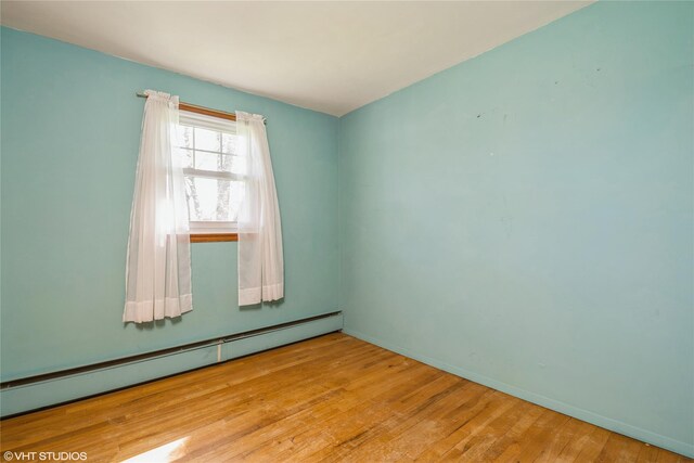 empty room featuring baseboards, a baseboard radiator, and wood finished floors
