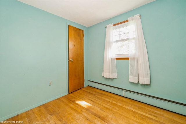 spare room featuring baseboards, a baseboard heating unit, and wood finished floors