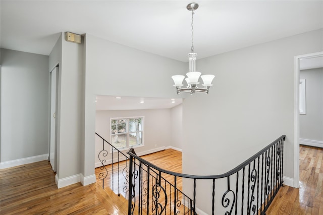 hall featuring baseboards, a chandelier, wood finished floors, and an upstairs landing
