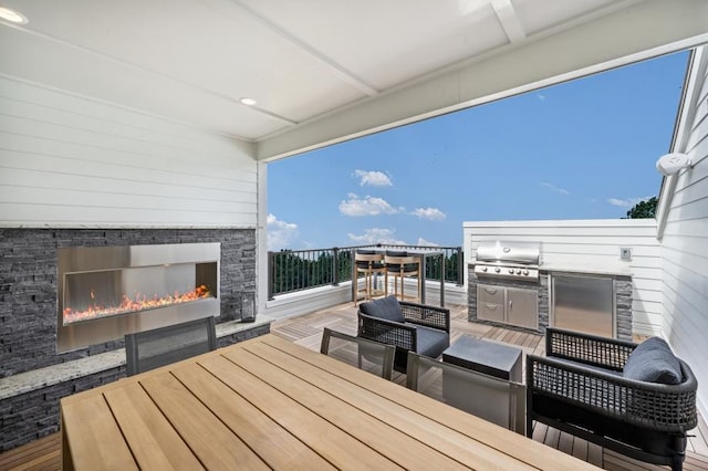 wooden deck with outdoor dining space, area for grilling, and a lit fireplace