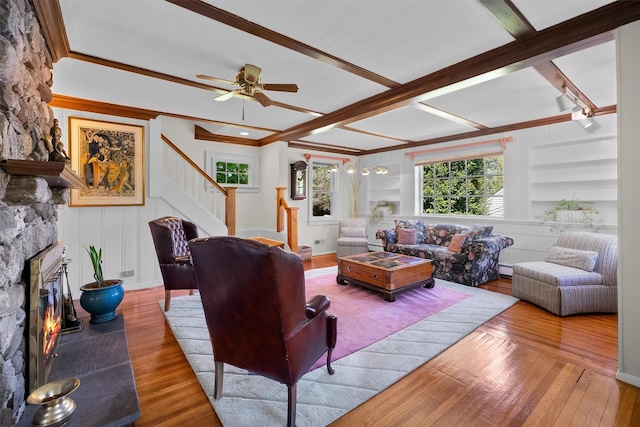 living area with wood-type flooring, crown molding, stairs, a fireplace, and ceiling fan