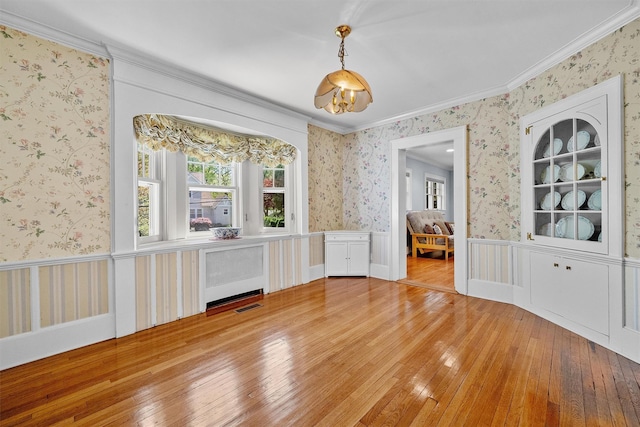 unfurnished dining area featuring visible vents, light wood finished floors, radiator, ornamental molding, and wallpapered walls