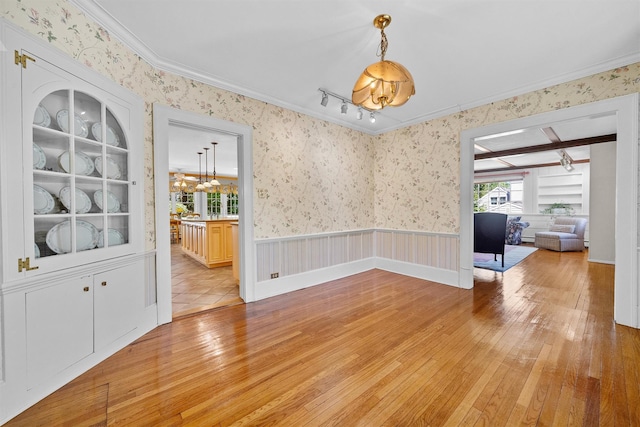 unfurnished dining area featuring wallpapered walls, an inviting chandelier, ornamental molding, and light wood finished floors