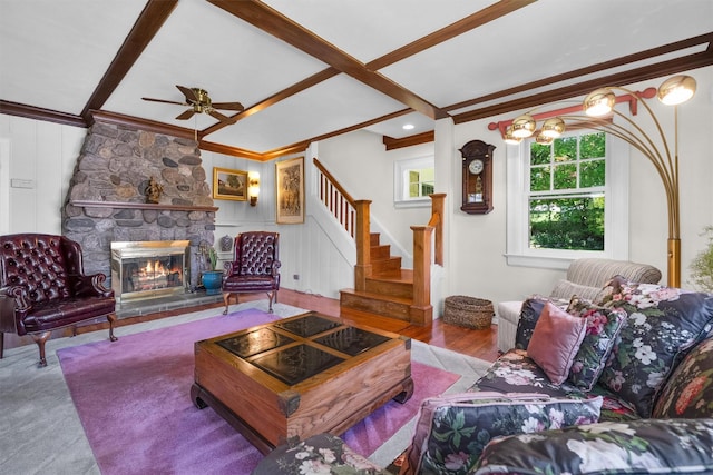 living area with beam ceiling, a fireplace, a ceiling fan, ornamental molding, and stairway
