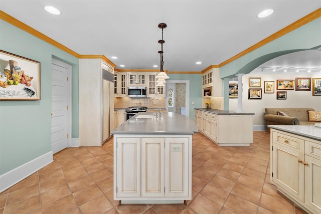 kitchen featuring decorative columns, a sink, appliances with stainless steel finishes, and cream cabinetry