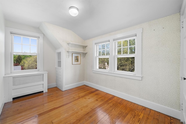 bonus room with baseboards, light wood-style flooring, radiator, and vaulted ceiling