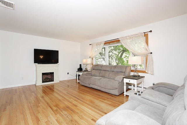 living area with light wood-style floors, a glass covered fireplace, baseboard heating, and baseboards