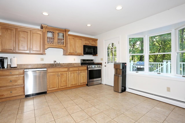 kitchen featuring stainless steel appliances, a sink, a baseboard radiator, dark stone counters, and light tile patterned floors