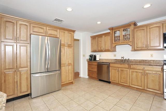 kitchen with appliances with stainless steel finishes, stone counters, recessed lighting, light tile patterned floors, and glass insert cabinets