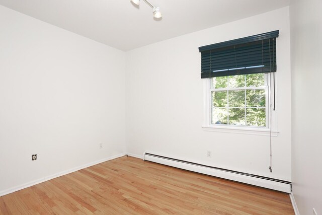 empty room featuring a baseboard radiator, light wood-type flooring, and baseboards