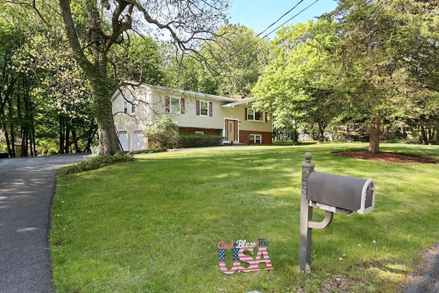 raised ranch featuring a garage, asphalt driveway, and a front yard
