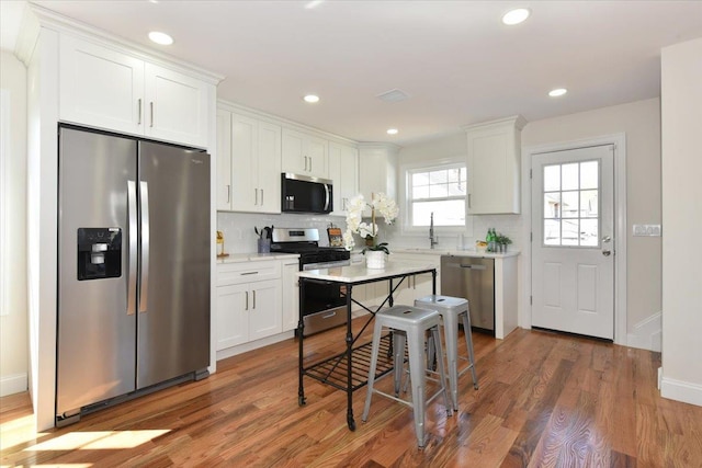 kitchen with appliances with stainless steel finishes, wood finished floors, decorative backsplash, and white cabinets