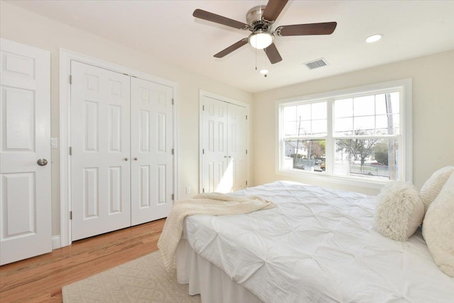 bedroom with recessed lighting, wood finished floors, two closets, ceiling fan, and visible vents