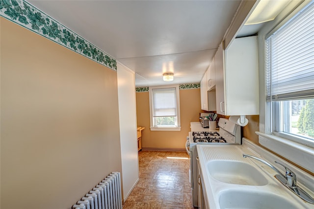 kitchen featuring white gas stove, radiator heating unit, a sink, light countertops, and white cabinets