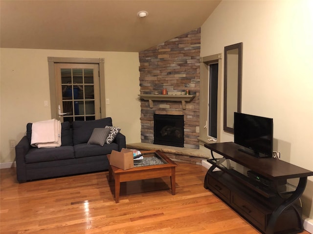 living room with a stone fireplace, light wood-type flooring, and vaulted ceiling