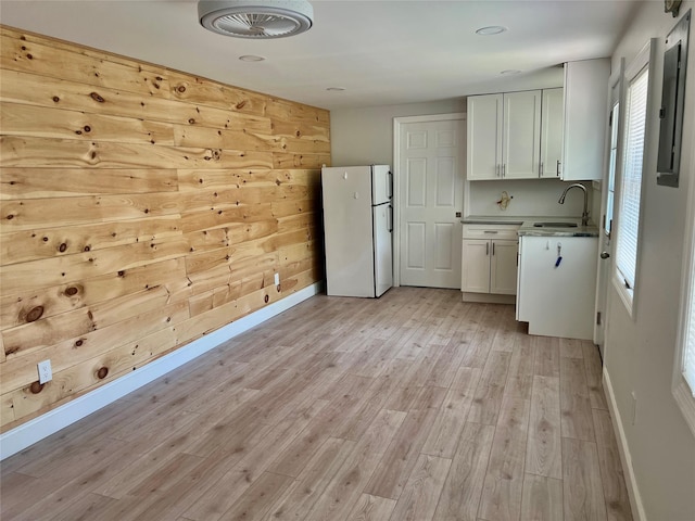 kitchen with freestanding refrigerator, baseboards, white cabinets, and a sink